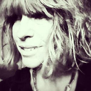 Close-up portrait of a person with bangs and tousled hair, smiling softly; black-and-white image.